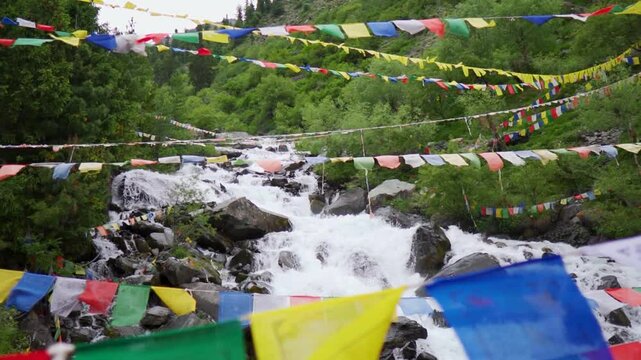 Slow motion shot of a water stream in the Himalayan mountains with prayer flags waving above it as seen near Triloknath village in Pattan valley, Himachal Pradesh, India. Scenic view of waterfall. 