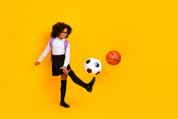 Playful schoolgirl kicking soccer ball on yellow background, representing education, sports, and...