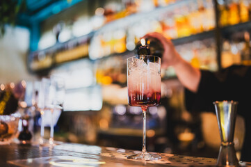 Bartender pouring a refreshing cocktail into a tall glass with ice cubes at a stylish bar. Vibrant...