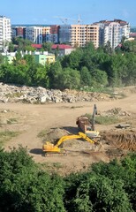 Crane and construction site, process of building a new building. Yellow excavator digs a pit for the construction of a multi-story building in a residential area. Ivano-Frankivsk, Ukraine