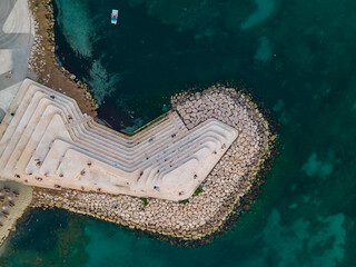 Drone top-down image of a contemporary coastal promenade featuring tiered concrete seating...