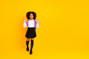 Cheerful schoolgirl with backpack gestures in a uniform standing against vibrant yellow reflective...