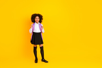 Cheerful schoolgirl with a backpack posing confidently in uniform on a vibrant yellow background...
