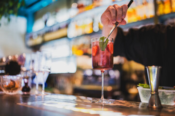 Bartender preparing a refreshing strawberry cocktail with ice and mint in a tall glass at a stylish...