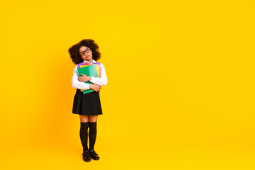 Charming schoolgirl in uniform holding colorful book on yellow background representing education...