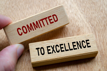 Fingers align wooden blocks that declare commitment to EXCELLENCE, reinforcing an unshakable focus...