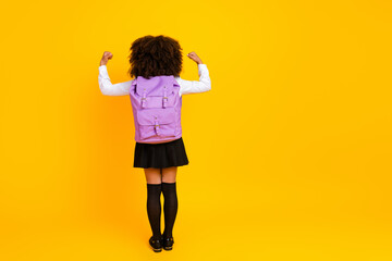 Confident schoolgirl showing strength symbol in stylish uniform on vibrant yellow background with schoolbag