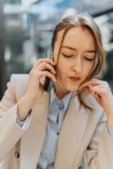 Professional woman in a beige blazer using a smart phone, expressing focus and engagement. Urban...