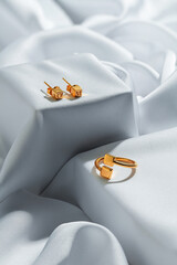 Gold earrings and a ring are artfully arranged on smooth silk, showcasing a modern design with...