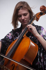 Woman playing cello, wearing floral robe, studio shot.
