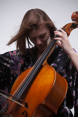 Woman playing cello, wearing floral kimono, studio shot.