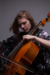 Woman playing cello, wearing floral kimono, studio shot.
