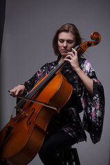 Woman playing cello, wearing floral kimono, studio shot.