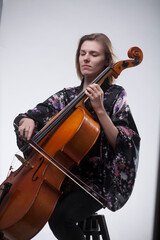 Woman playing cello, wearing floral robe, eyes closed.