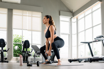 Fototapeta premium A woman is lifting weights in a gym. She is wearing a black tank top and black pants