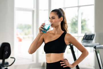 A woman is drinking water from a glass. She is wearing a black tank top. The glass is blue