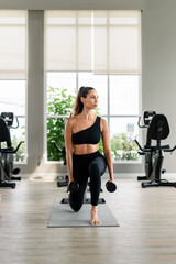 Fototapeta premium A woman is doing a workout in a gym. She is holding two dumbbells and is squatting down