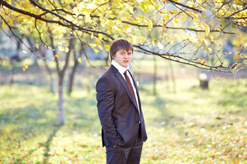 A man in a suit and tie stands in a park with trees in the background