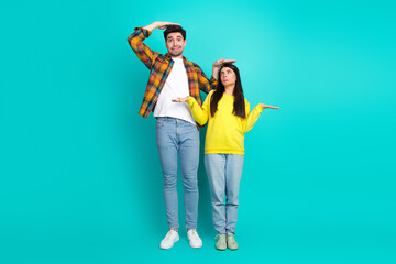 Young couple playfully comparing heights against a teal background, expressing joy and fun