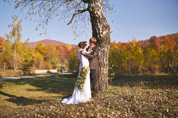 A couple is standing under a tree, with the bride holding a bouquet