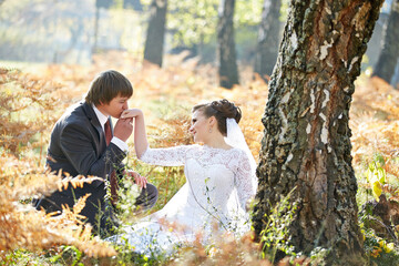 A bride and groom are sitting under a tree in a field