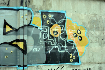 A drawing, graffiti depicting the word MASSL is painted on a yellow background on a white, gray concrete fence. Blue, pink, gray, and dark gray letters and black lines, with black shadows.