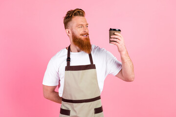 Young red-haired barista holding a disposable coffee cup against pink background, showcasing casual style and confidence in a leisure setting