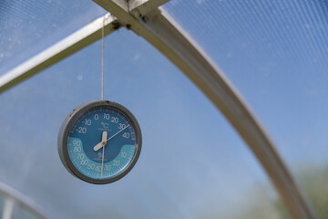 Analog thermometer and hygrometer hanging inside a plastic greenhouse.