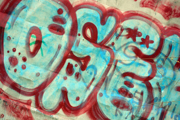 White, blue letters with red dashes, dots, circles, and lines with thick red borders. A drawing or graffiti depicting word OSEK is painted on a white-gray concrete fence.