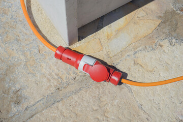 Attaching an orange extension cord for outdoor power, showing a red and white industrial electrical...
