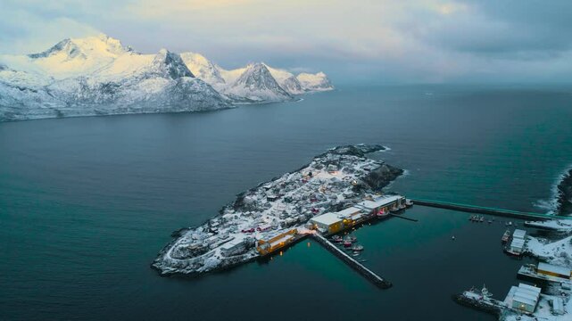 Fischerboot verl&auml;sst zur blauen Stunde den Hafen von Hus&oslash;y auf Senja in Norwegen, Lichter der Siedlung spiegeln sich im Wasser, winterliche Stimmung &uuml;ber dem ruhigen Nordmeer