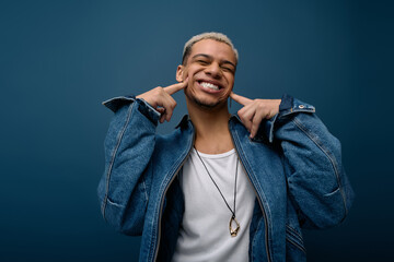 Young man showcases style in denim jacket against a vibrant blue backdrop