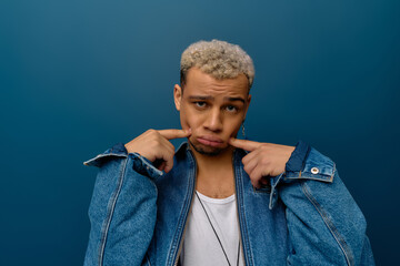 Confident young man in a stylish denim jacket poses against a blue background