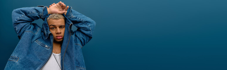 Young man with stylish denim jacket poses confidently against a blue background