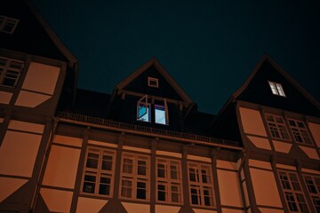 Illuminated attic window with open shutters in a half-timbered house at night, emitting cool light...