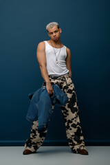 Stylish young man with dyed hair showcases denim fashion against blue backdrop