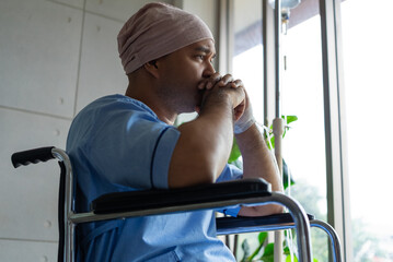Asian man cancer patient sitting alone in wheelchair looking outside window in hospital ward with...