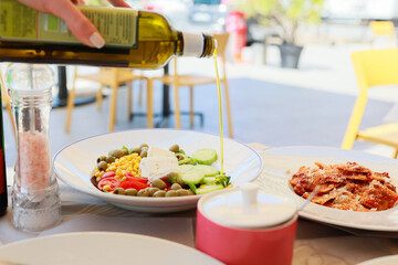 Fresh salad on a terrace table in Italy, with a hand pouring olive oil over the greens.