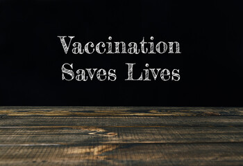 Vaccination saves lives text on black and white wooden background.