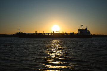A ship drifts along the Mississippi River, silhouetted against the glowing orange and gold hues of...