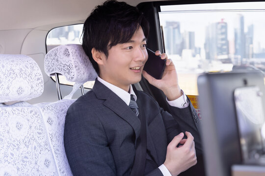 タクシーの後部座席に座りスマホで話すビジネスマン