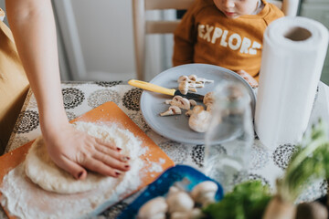 A parent and child work together to prepare pizza, featuring fresh mushrooms and rolled dough, in a...