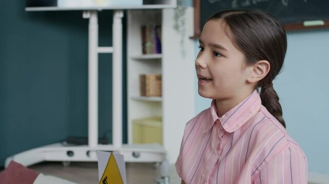 Young Asian student with traffic signs in hand explaining road safety and awareness rules to classmates during interactive activity in modern classroom