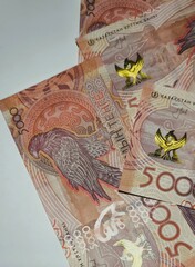 A macro shot of 5000 tenge banknotes from Kazakhstan displays intricate design details, including a bird and traditional patterns