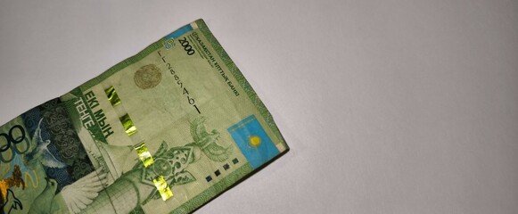 A partially visible 2000 tenge note from Kazakhstan lies on a white surface, showing national...