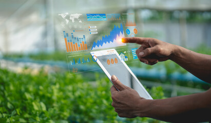 A person uses a tablet displaying augmented reality charts and graphs over a green agricultural field, illustrating technology in farming and data analysis.