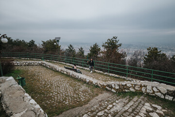 Two people spend time together in a serene natural setting, standing and sitting by a railing...