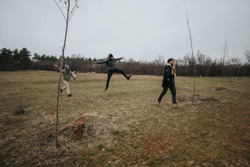 Three people engage in joyful movements and exploration within a natural outdoor environment. The...