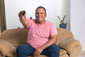A man in a red shirt is sitting on a couch and holding a remote control