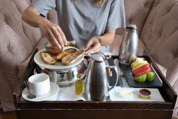 Adult woman enjoying breakfast with fruit and coffee in a hotel room, spreading toast with extra virgin olive oil.